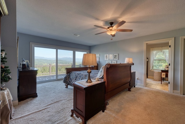 bedroom with a mountain view, light carpet, ceiling fan, access to exterior, and a textured ceiling