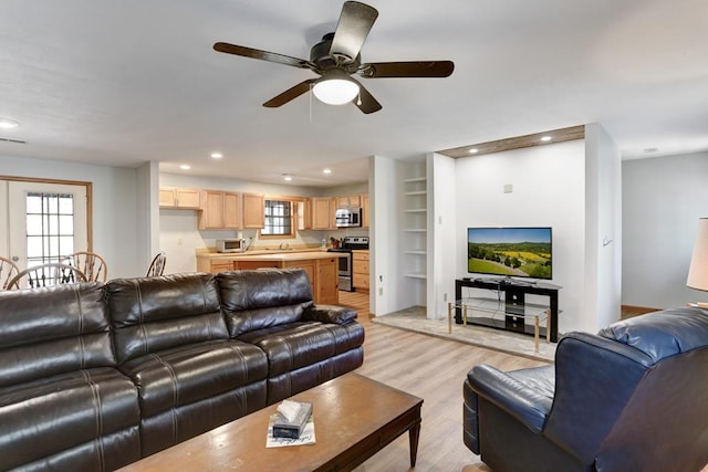 living room with built in shelves, a healthy amount of sunlight, ceiling fan, and light wood-type flooring