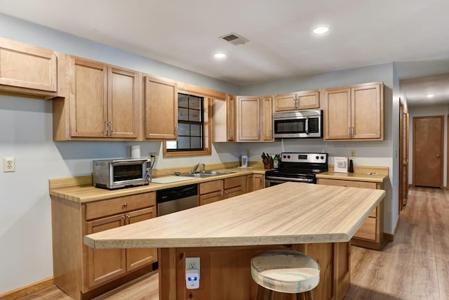 kitchen with sink, appliances with stainless steel finishes, a center island, and light hardwood / wood-style flooring