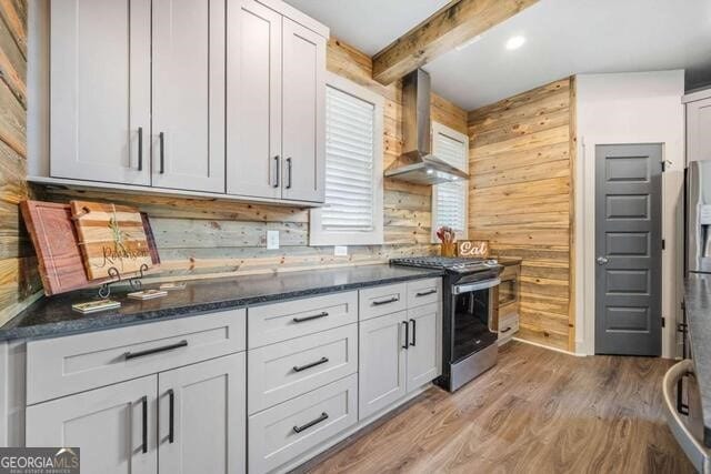 kitchen featuring beam ceiling, wooden walls, wall chimney exhaust hood, and stainless steel range oven