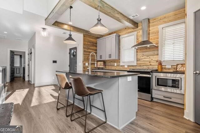 kitchen with wall chimney exhaust hood, stainless steel appliances, sink, decorative light fixtures, and a center island