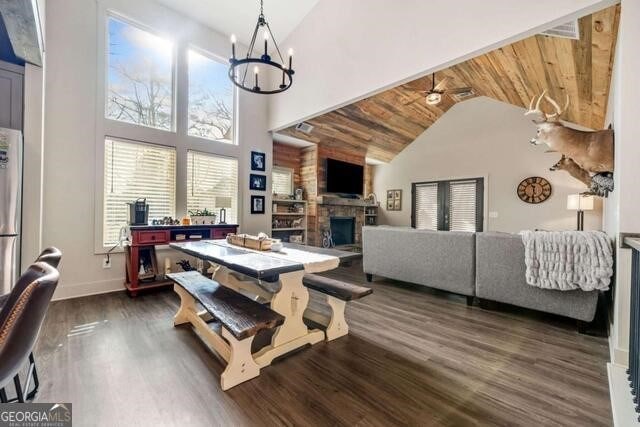 dining room with dark hardwood / wood-style flooring, wood ceiling, ceiling fan with notable chandelier, high vaulted ceiling, and a fireplace