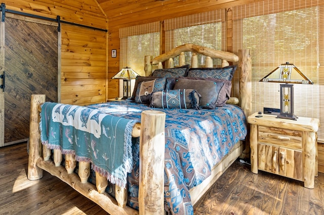 bedroom with wooden walls, dark hardwood / wood-style floors, and a barn door