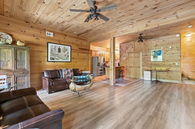 living room with ceiling fan, wooden walls, light hardwood / wood-style floors, and wooden ceiling