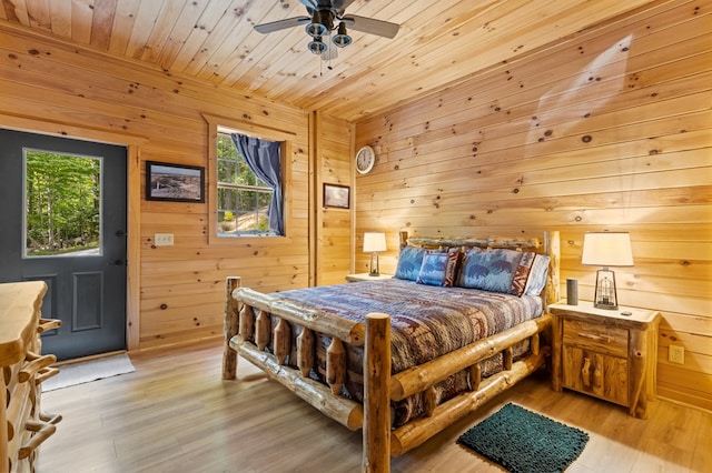 bedroom featuring light hardwood / wood-style floors, wooden walls, and ceiling fan