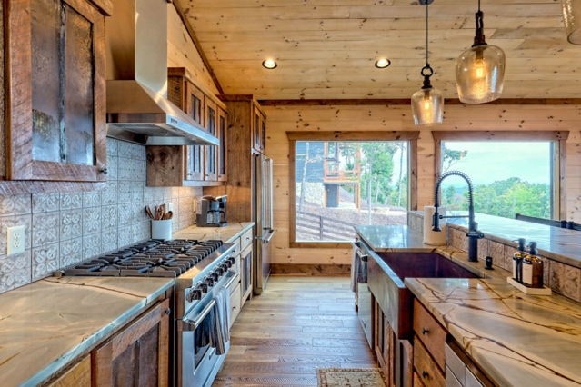 kitchen with decorative backsplash, light hardwood / wood-style floors, wall chimney range hood, appliances with stainless steel finishes, and decorative light fixtures