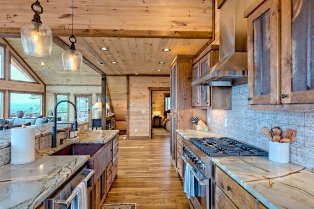 kitchen with wall chimney range hood, light hardwood / wood-style floors, decorative light fixtures, light stone counters, and appliances with stainless steel finishes