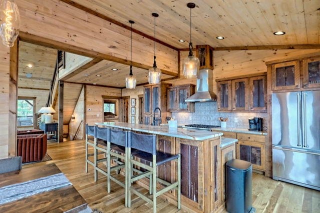 kitchen featuring an island with sink, lofted ceiling, wall chimney exhaust hood, stainless steel refrigerator, and light wood-type flooring