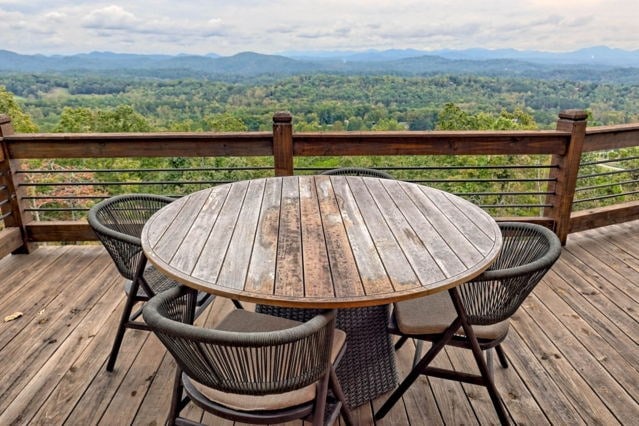 wooden terrace featuring a forest view, a mountain view, and outdoor dining space