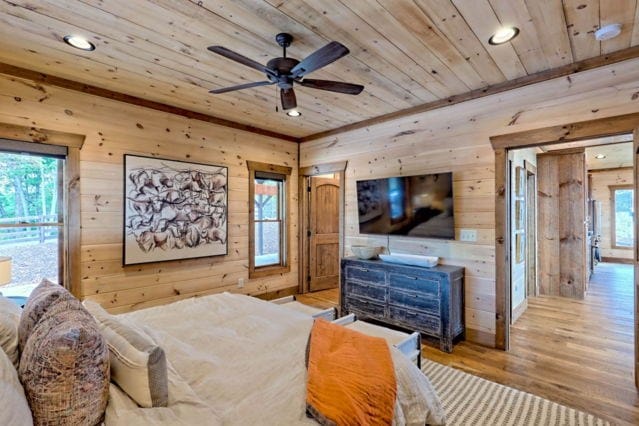 bedroom featuring wooden walls, light hardwood / wood-style floors, wood ceiling, and multiple windows