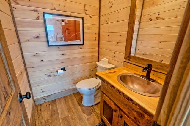 half bathroom with wooden walls, vanity, toilet, and wood finished floors