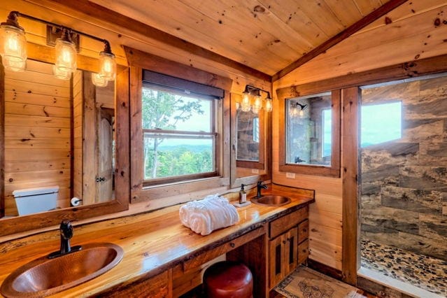 bathroom featuring wooden ceiling, a sink, vaulted ceiling, and wooden walls