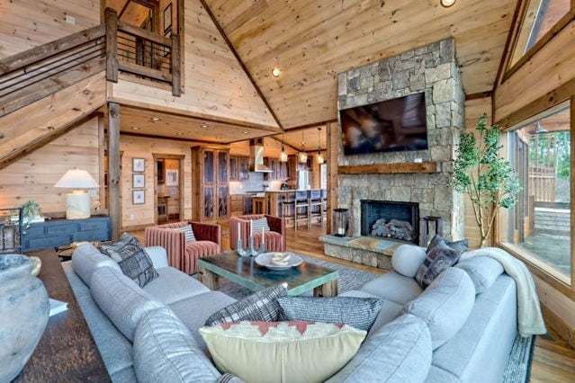 living area with wooden ceiling, a stone fireplace, wooden walls, wood finished floors, and high vaulted ceiling