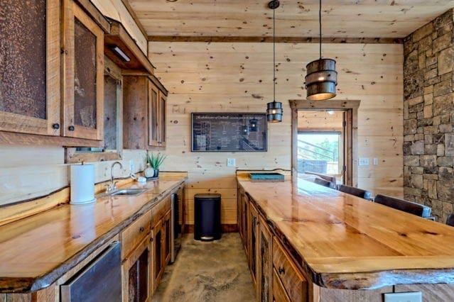 bar featuring pendant lighting, concrete floors, wood ceiling, a sink, and wooden walls