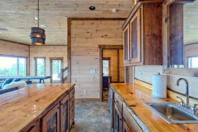 kitchen with wood walls, hanging light fixtures, butcher block countertops, and sink