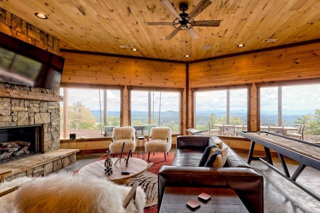 living room with ceiling fan, a mountain view, wood walls, a stone fireplace, and wooden ceiling