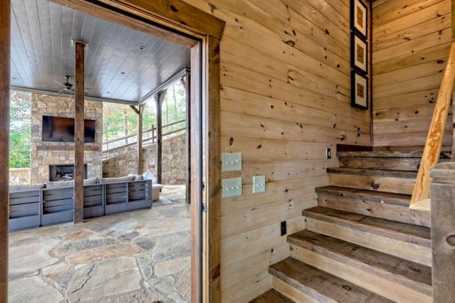 stairs featuring wooden walls, a stone fireplace, wooden ceiling, and ceiling fan