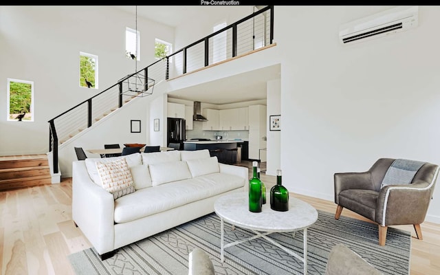 living room featuring light hardwood / wood-style floors, a towering ceiling, a wall mounted air conditioner, and an inviting chandelier