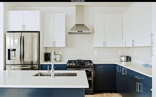 kitchen featuring light hardwood / wood-style floors, wall chimney range hood, backsplash, blue cabinetry, and stainless steel appliances