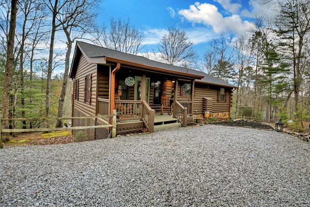 view of front of house with gravel driveway, covered porch, a shingled roof, and fence