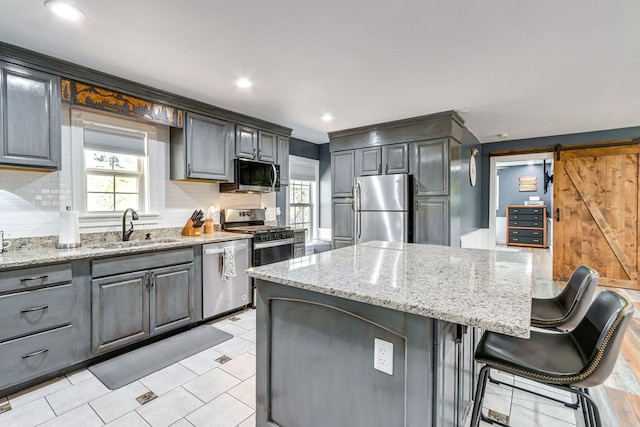 kitchen with appliances with stainless steel finishes, a breakfast bar, tasteful backsplash, sink, and a barn door