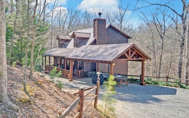 view of property exterior featuring metal roof, a view of trees, a chimney, and fence