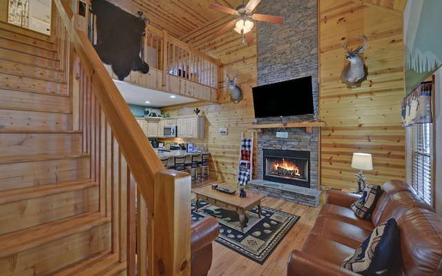 living area with stairs, hardwood / wood-style flooring, a stone fireplace, a towering ceiling, and wood walls