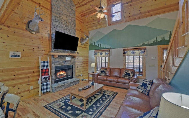 living area featuring a stone fireplace, stairs, ceiling fan, and wood finished floors