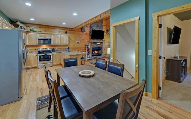 dining area with recessed lighting, light wood-style flooring, a stone fireplace, and wood walls