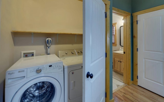 clothes washing area with laundry area, washing machine and dryer, and light wood-type flooring