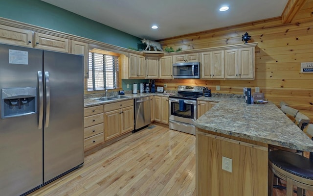 kitchen with a peninsula, a sink, appliances with stainless steel finishes, a kitchen bar, and light wood-type flooring