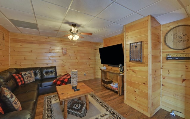 living area featuring a drop ceiling, wood finished floors, a ceiling fan, and wood walls