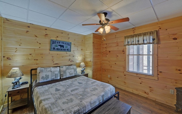 bedroom with a drop ceiling, wood finished floors, and wood walls