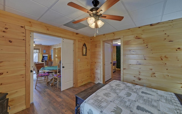 bedroom featuring a drop ceiling, dark wood-type flooring, and wood walls