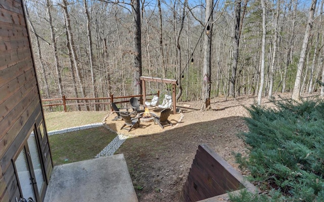 view of yard featuring a view of trees, a fire pit, and fence