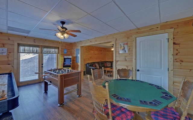 recreation room with a ceiling fan, wood finished floors, wood walls, and a paneled ceiling