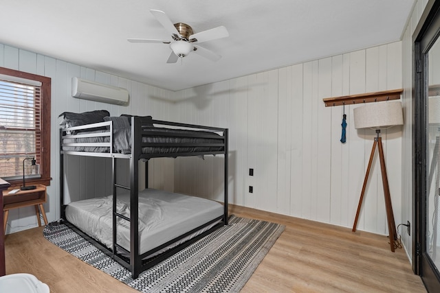 bedroom with ceiling fan, wood finished floors, and a wall mounted AC