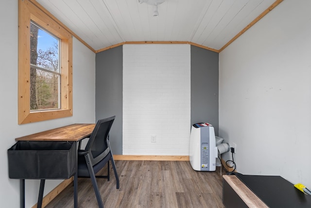 home office featuring baseboards, lofted ceiling, brick wall, wood finished floors, and crown molding