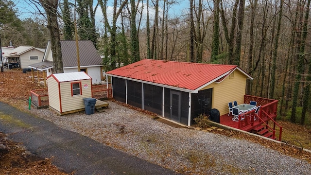 exterior space with an outbuilding, metal roof, a deck, and a sunroom