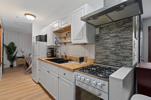 kitchen with butcher block countertops, under cabinet range hood, stainless steel range with gas cooktop, white cabinetry, and a sink