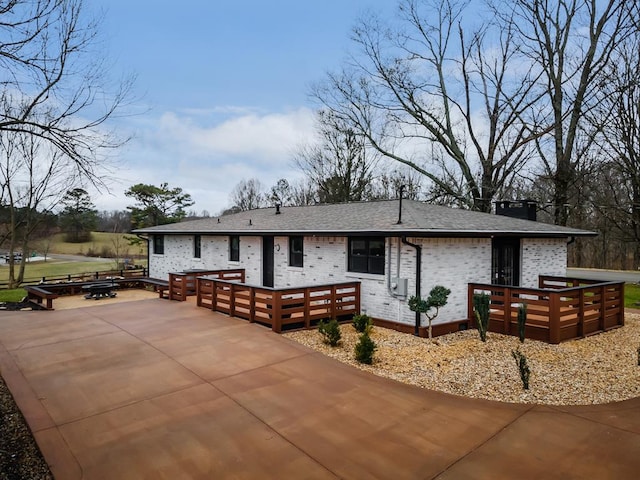 view of front of home with an outdoor fire pit, brick siding, concrete driveway, roof with shingles, and a patio area