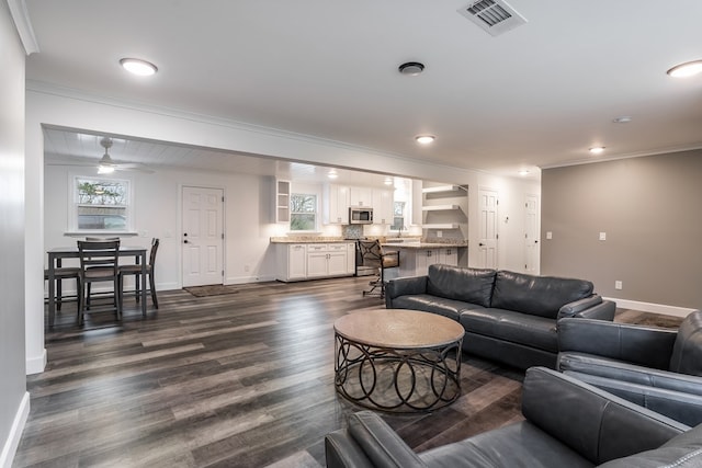 living area with ornamental molding, dark wood-style flooring, visible vents, and baseboards