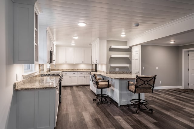 kitchen featuring ornamental molding, light stone countertops, stainless steel appliances, a kitchen bar, and white cabinetry