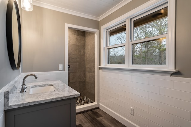 bathroom featuring ornamental molding, wainscoting, a tile shower, vanity, and wood finished floors