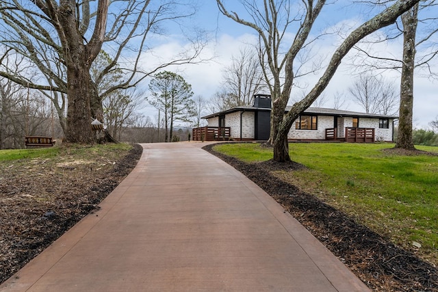 view of property exterior featuring concrete driveway, brick siding, a lawn, and a chimney