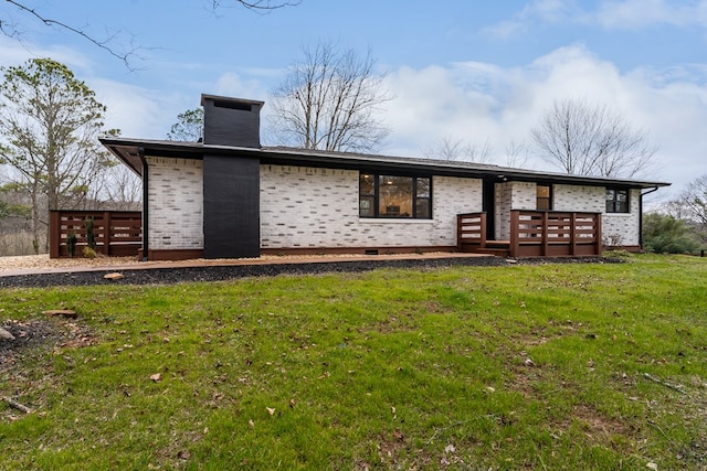 rear view of property with crawl space, a lawn, a chimney, and brick siding