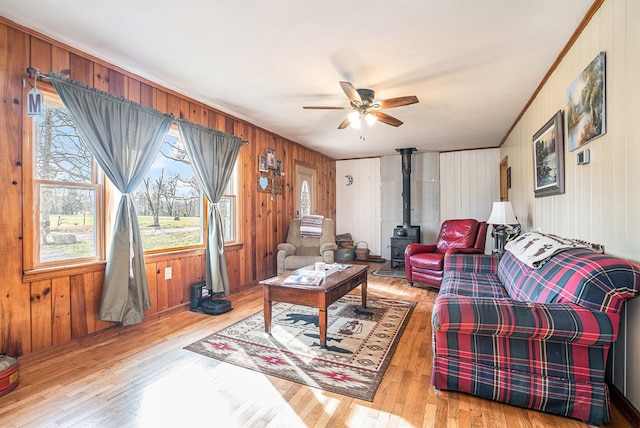 living room featuring crown molding, light hardwood / wood-style flooring, ceiling fan, wooden walls, and a wood stove