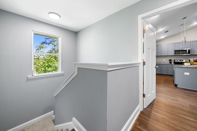 stairway with baseboards, visible vents, wood finished floors, and lofted ceiling