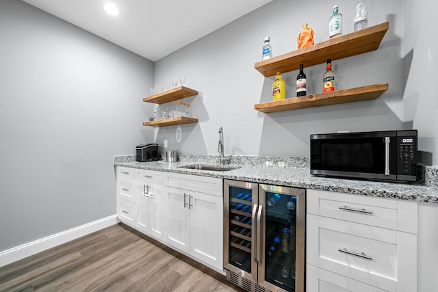 bar featuring wood finished floors, beverage cooler, baseboards, a sink, and wet bar