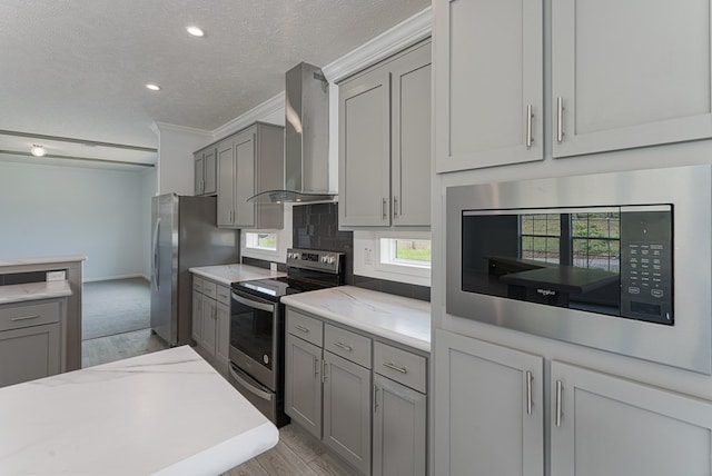 kitchen featuring wall chimney exhaust hood, gray cabinets, a textured ceiling, appliances with stainless steel finishes, and light hardwood / wood-style floors